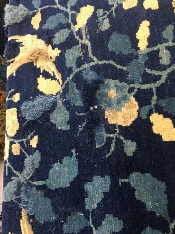Close-up of a navy rug featuring light blue and cream floral patterns with damaged and frayed areas.