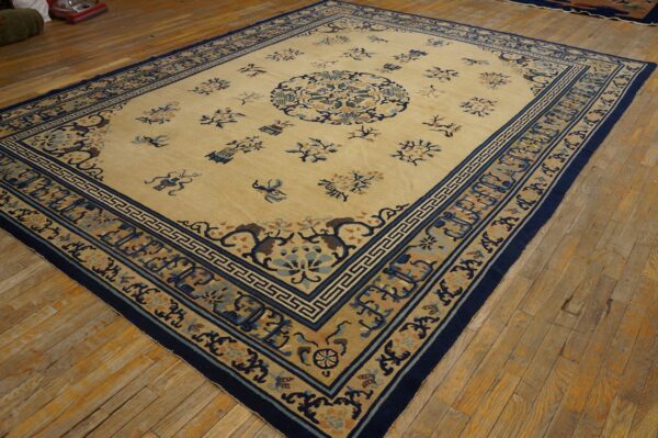Pale yellow rug with blue floral motifs and a detailed geometric navy border on rustic wood floors.