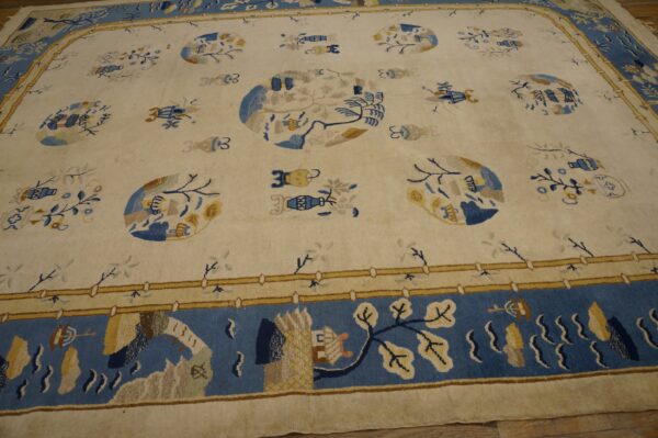 Cream rug with blue and gold scattered botanical and medallion designs, framed by a wide blue pictorial border.