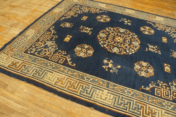 Navy blue rug with tan, cream, and light blue geometric borders displayed on light wood plank flooring.