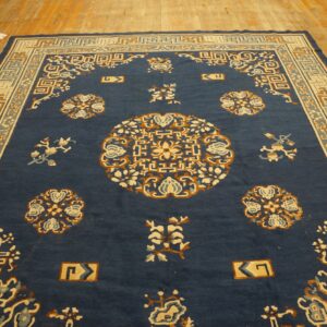 Navy blue rug with cream and rust traditional motifs on a worn light wood plank floor.