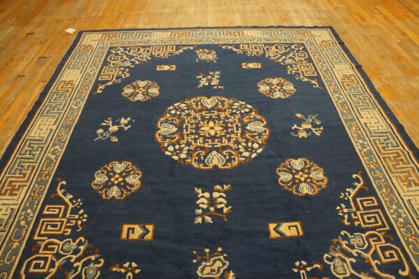 Navy blue rug with cream and rust traditional motifs on a worn light wood plank floor.
