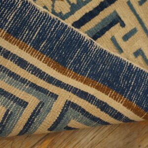 Textured rug displaying blue, brown, and beige interlocking geometric patterns, folded over wood planks.