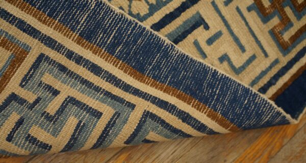 Textured rug displaying blue, brown, and beige interlocking geometric patterns, folded over wood planks.