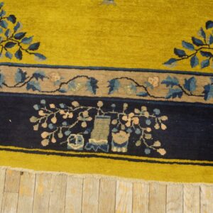 Chartreuse and navy rug border with floral and vase motifs lies on weathered wood floorboards.