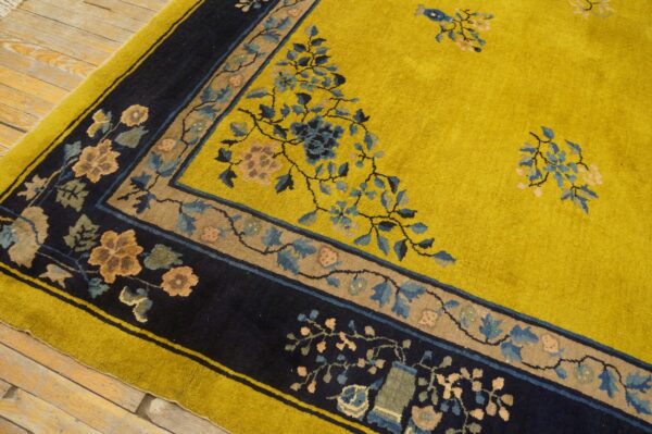 The high-pile yellow rug has a wide dark border with tan panels and blue floral motifs on wood flooring.