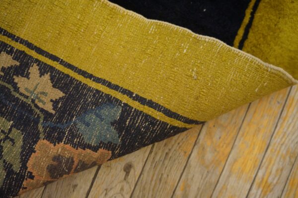 A curled rug displays a dark, patterned face with colorful motifs and a bright yellow reverse side on wood floors.