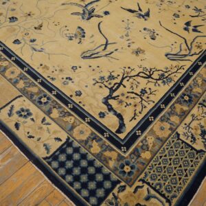Beige rug featuring blue and brown botanical patterns and birds, bordered by geometric panels, resting on wood flooring.