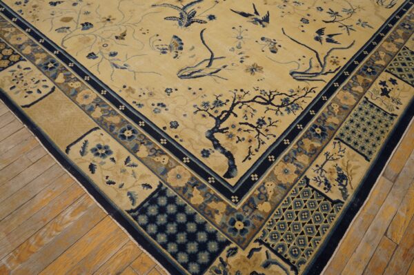 Beige rug featuring blue and brown botanical patterns and birds, bordered by geometric panels, resting on wood flooring.