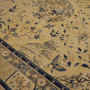 Low-pile golden rug with blue birds and branches, showing a patterned border on light wood floorboards.