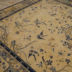 Gold and blue rug featuring birds and vines rests on natural wood plank flooring.
