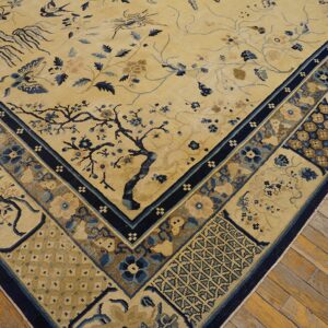 Pale yellow rug corner with a dense border and blue botanical motifs rests on distressed wood flooring.