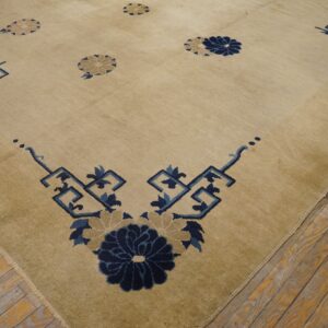 Beige rug with deep blue stylized florals and geometric corner patterns on rustic plank wood flooring.