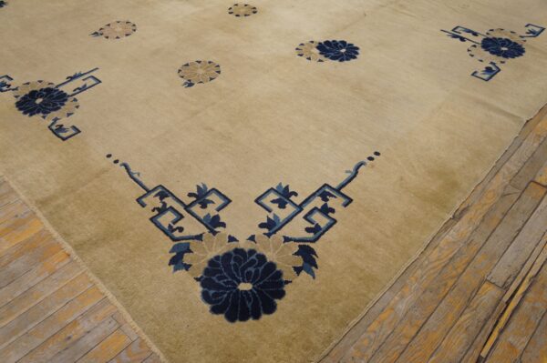 Beige rug with deep blue stylized florals and geometric corner patterns on rustic plank wood flooring.