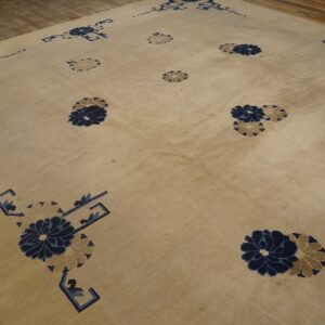 Tan rug with stylized blue and beige floral patterns and geometric corner accents on wood floor.