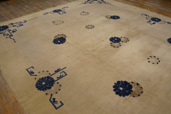 Tan rug with stylized blue and beige floral patterns and geometric corner accents on wood floor.