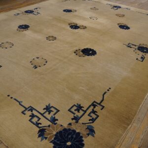 Low-pile tan area rug with scattered navy floral medallions and corner fretwork on wood flooring.