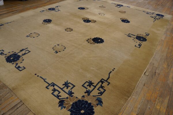 Low-pile tan area rug with scattered navy floral medallions and corner fretwork on wood flooring.