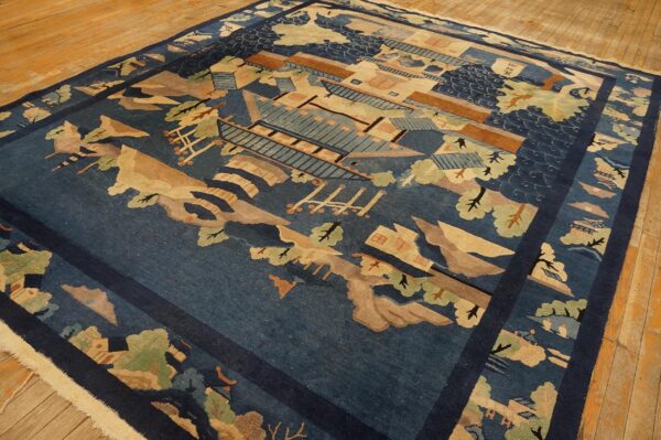 Deep indigo scenic rug with tan, green, and brown architectural and landscape elements on wood plank flooring.