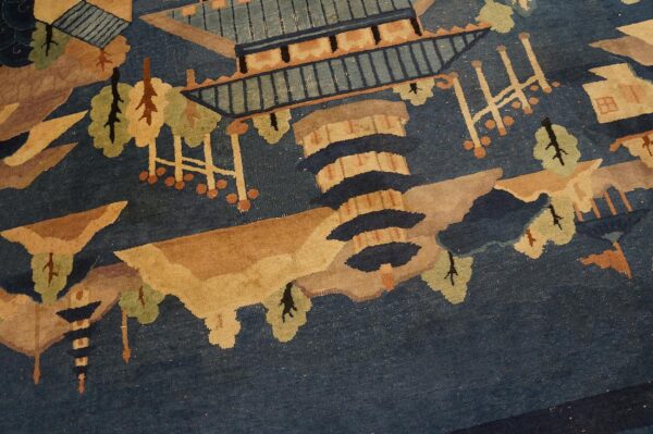 Blue pictorial rug detail featuring tan pagodas, stylized green trees, and brown landscape elements.