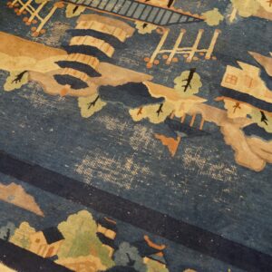 Blue rug detail showing a scenic pattern in beige and green with significant pile wear exposing the backing.