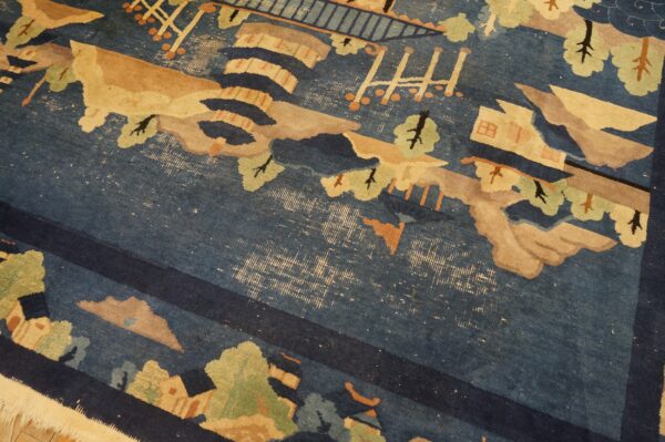 Blue rug detail showing a scenic pattern in beige and green with significant pile wear exposing the backing.