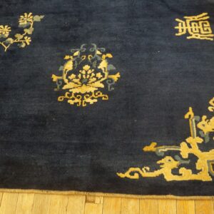 Dark blue rug with gold and teal scattered floral and symbolic motifs on light wood flooring.