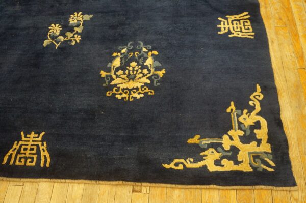 Dark blue rug with gold and teal scattered floral and symbolic motifs on light wood flooring.
