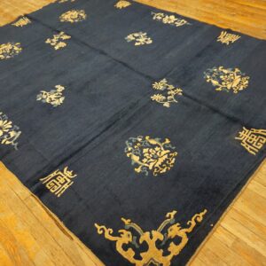 Dark indigo rug with scattered gold and gray-blue motifs laid diagonally on light brown wood floor.