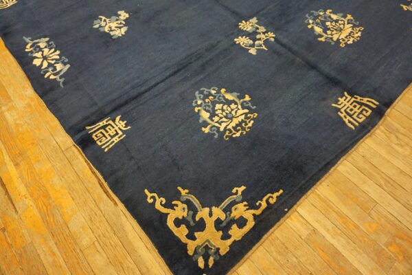 A navy blue rug with gold and gray floral and character motifs rests on worn light wood floorboards.