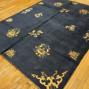 Large navy rug with scattered gold floral designs and corner brackets displayed on distressed wood flooring.