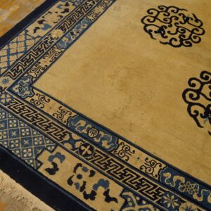 Golden tan rug featuring navy blue scrolling field motifs and detailed geometric borders on a wood floor.