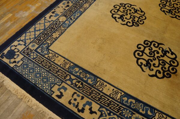 Golden tan rug featuring navy blue scrolling field motifs and detailed geometric borders on a wood floor.