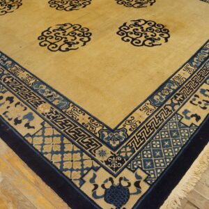 Detailed view of a golden yellow rug with navy and blue traditional border patterns on wood flooring.