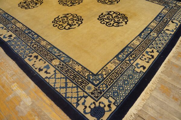 Detailed view of a golden yellow rug with navy and blue traditional border patterns on wood flooring.