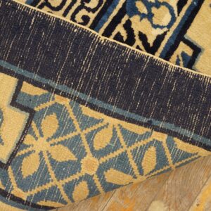 Gold, teal, and navy patterned rug folded to show the tightly woven reverse side on distressed wooden floorboards.