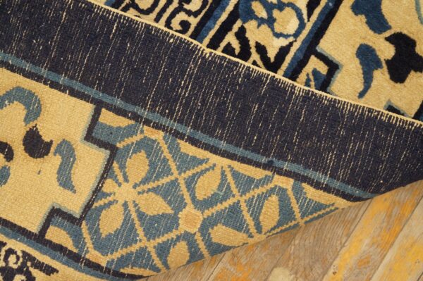 Gold, teal, and navy patterned rug folded to show the tightly woven reverse side on distressed wooden floorboards.