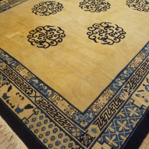 Golden yellow rug with dark blue swirling medallion motifs and a wide, complex geometric border on wood flooring.