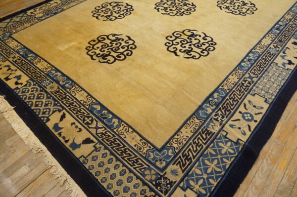 Golden yellow rug with dark blue swirling medallion motifs and a wide, complex geometric border on wood flooring.