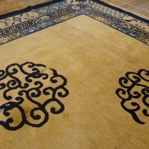 Tan field rug with two navy blue scrolling cloud patterns and multi-toned blue borders on wood floor.