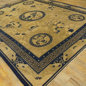 Golden tan rug with a navy blue Greek key border and traditional medallions on wooden floorboards.