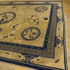 Golden rug with navy medallions and an elaborate Greek key border lies on worn wooden flooring.