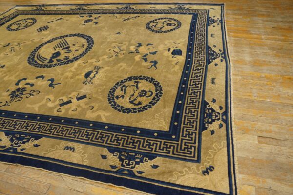 Golden rug with navy medallions and an elaborate greek key border lies on worn wooden flooring.
