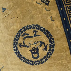 Detailed view of a gold and navy rug featuring a medallion with a mythical beast and geometric borders.