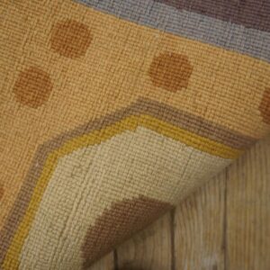 Flatweave rug features tan and brown polka dots with a border of yellow, gray, and purple stripes on wood flooring.