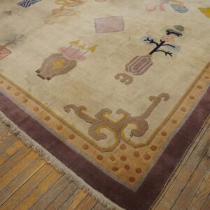 Muted beige rug featuring scattered symbolic designs and a multi-band border on worn wood plank flooring.
