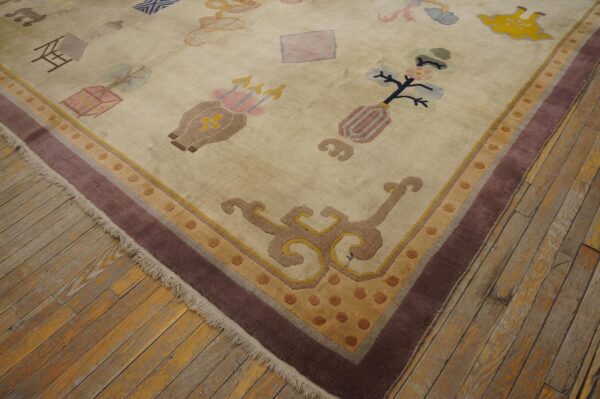 Muted beige rug featuring scattered symbolic designs and a multi-band border on worn wood plank flooring.