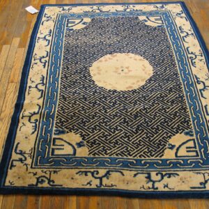 Blue and cream rug with a geometric maze pattern and round medallion centered on light hardwood floor.