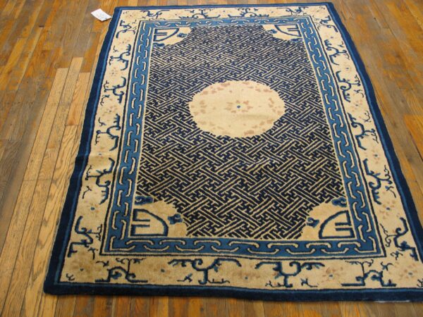 Blue and cream rug with a geometric maze pattern and round medallion centered on light hardwood floor.