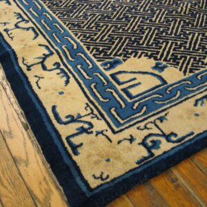 Tan and navy rug with geometric patterns and stylized borders rests on hardwood floors.